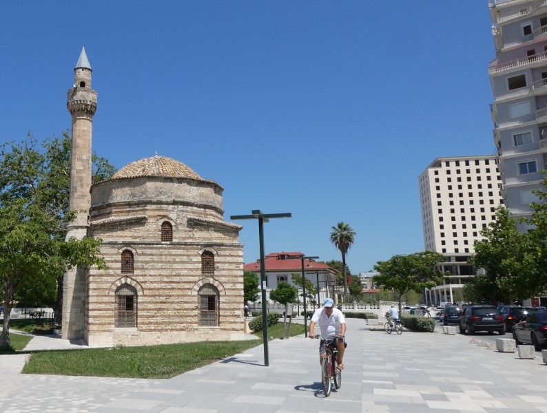 Oude moskee in moderne stadscentrum. Met ernaast een fietspad waar een man fietst